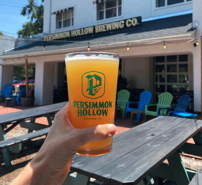 hand holding up persimmon hollow glass with beer